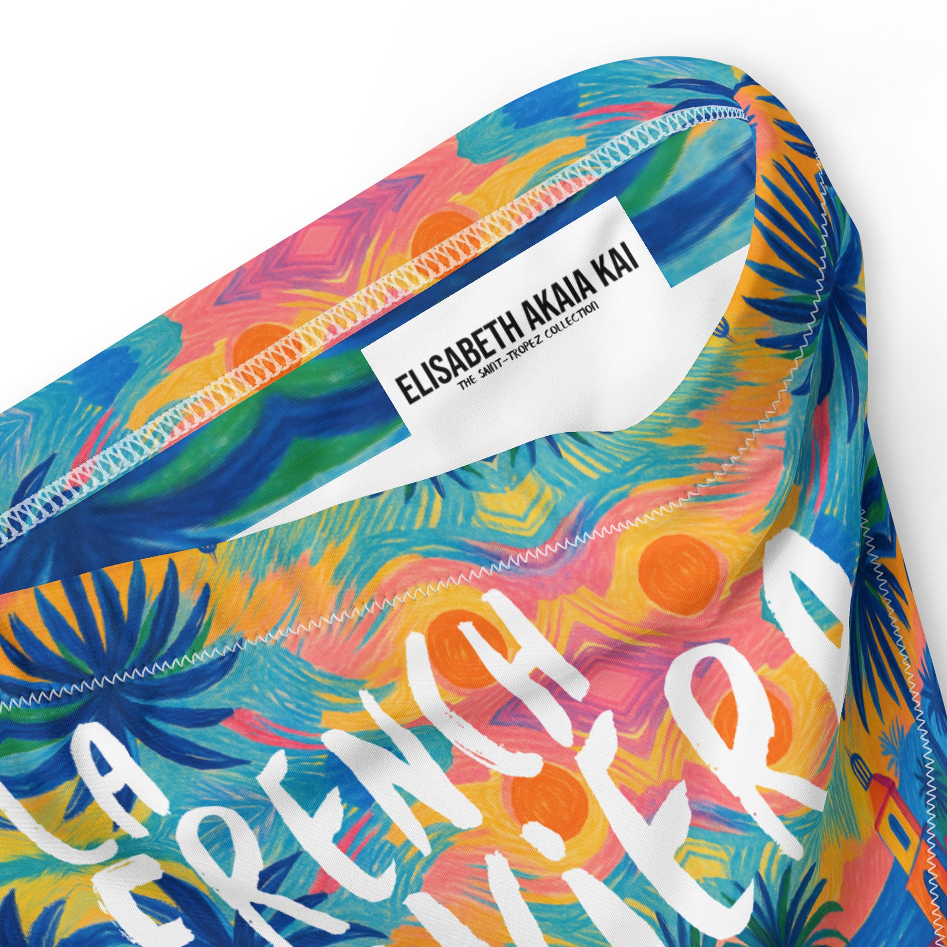 Vue detail d’un bas de bikini taille haute éco-responsable au motif tropical coloré (palmiers et maisons côtières), finition double couche et coutures zig-zag.