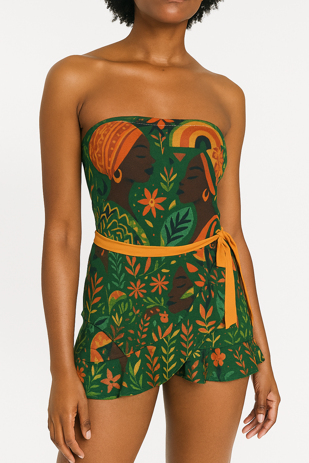 Femme noire portant l’ensemble Dzanaï composé d’un body bandeau et d’une jupe portefeuille courte à volants. Le tissu arbore un imprimé artistique vibrant aux motifs afro-méditerranéens dans des tons verts, orange et ocre. Photographie studio sur fond clair, mettant en valeur la silhouette et les détails du motif exclusif.