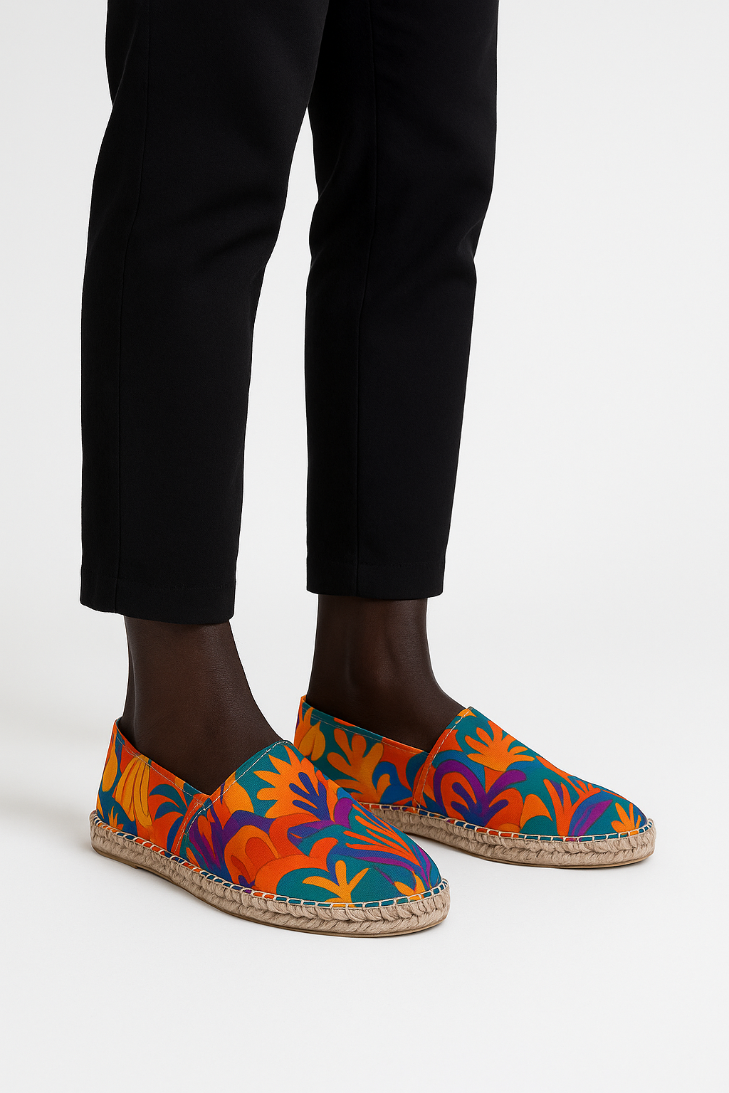 Espadrilles Palma Aurea aux motifs tropicaux colorés, portées par un mannequin afro vêtu d’un pantalon noir, sur fond neutre studio, mettant en avant le contraste chic et estival.