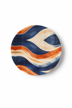 Assiette design en céramique de 16,5 cm de diamètre, motif ondulé peint à l’effet aquarelle, tons bleu profond, terracotta et sable, photographie produit sur fond blanc, art de la table contemporain et afro-luxe.