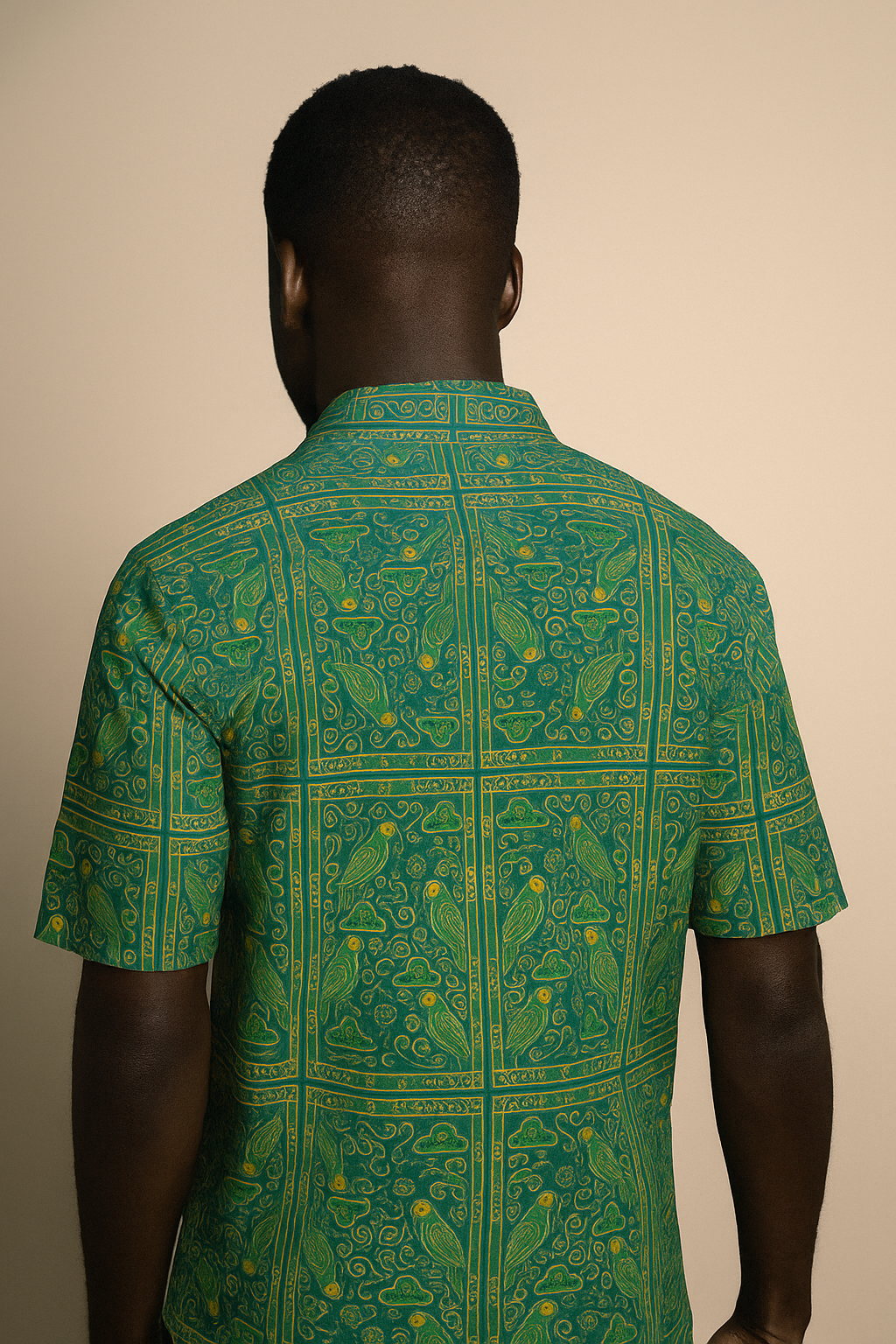 Homme afro élégant portant la chemise Okani de la collection Libreville Royale, vue de dos dans un studio photo à fond beige. Imprimé vert émeraude et or inspiré du patrimoine gabonais.