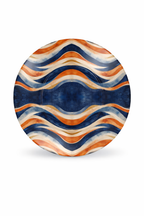 Assiette ronde en céramique design Mbeyla ornée d’un motif ondulé symétrique aux tons bleu profond, terracotta, sable et ivoire, photographiée sur fond blanc en format vertical, pièce d’art de la table afro-luxe inspirée des ondulations solaires et du design gabonais contemporain.