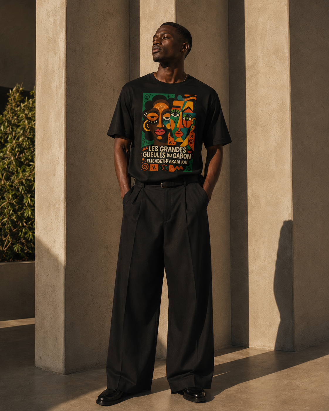 Homme africain en t-shirt noir graphique Les Grandes Gueules du Gabon dans une architecture minérale, univers afro luxe contemporain.
