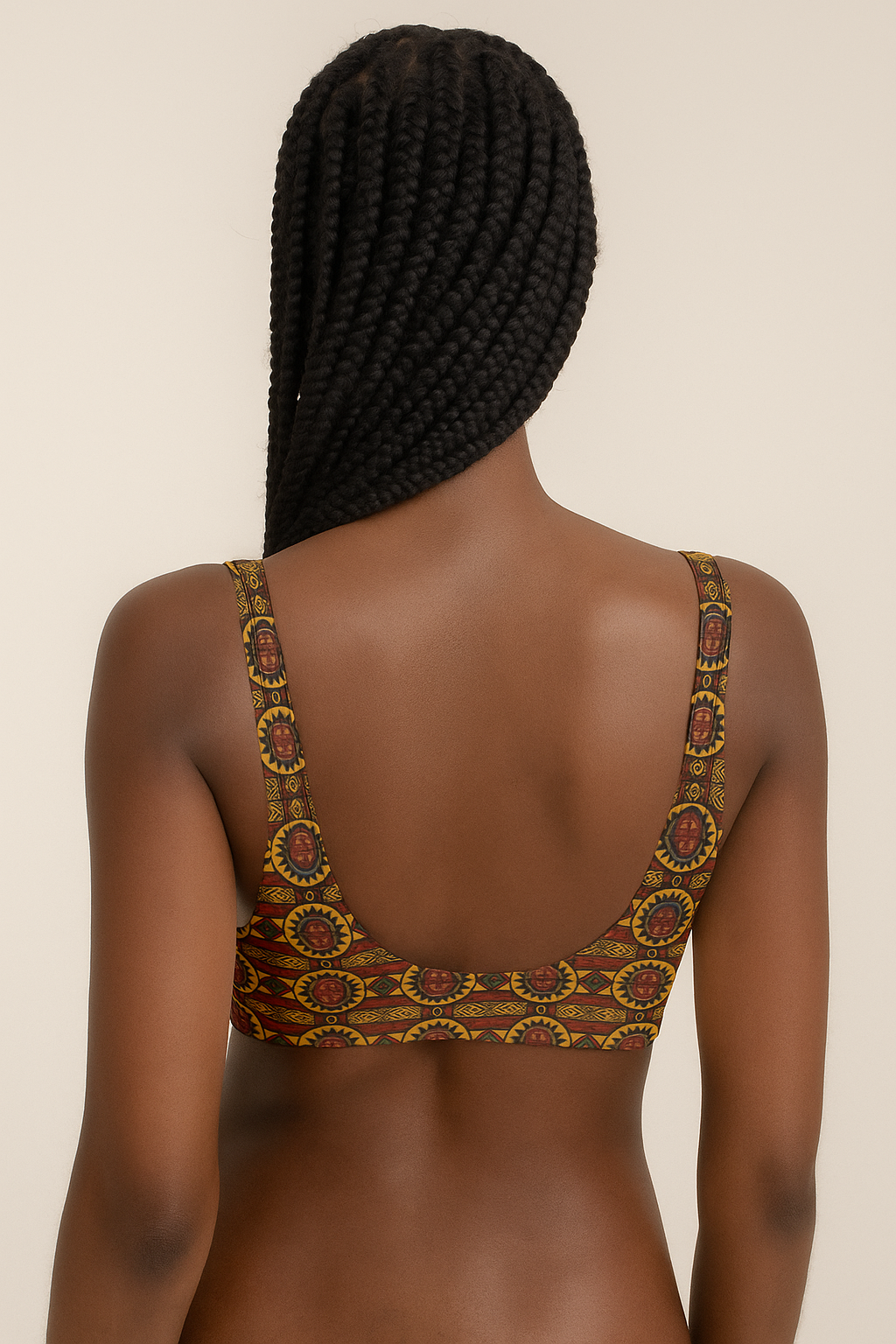 Vue arrière d’une mannequin afro aux longues tresses portant le haut de maillot de bain éco-responsable Kaya Lumina, rembourré, orné d’un imprimé géométrique africain doré, rouge et noir, en studio sur fond neutre beige avec lumière douce