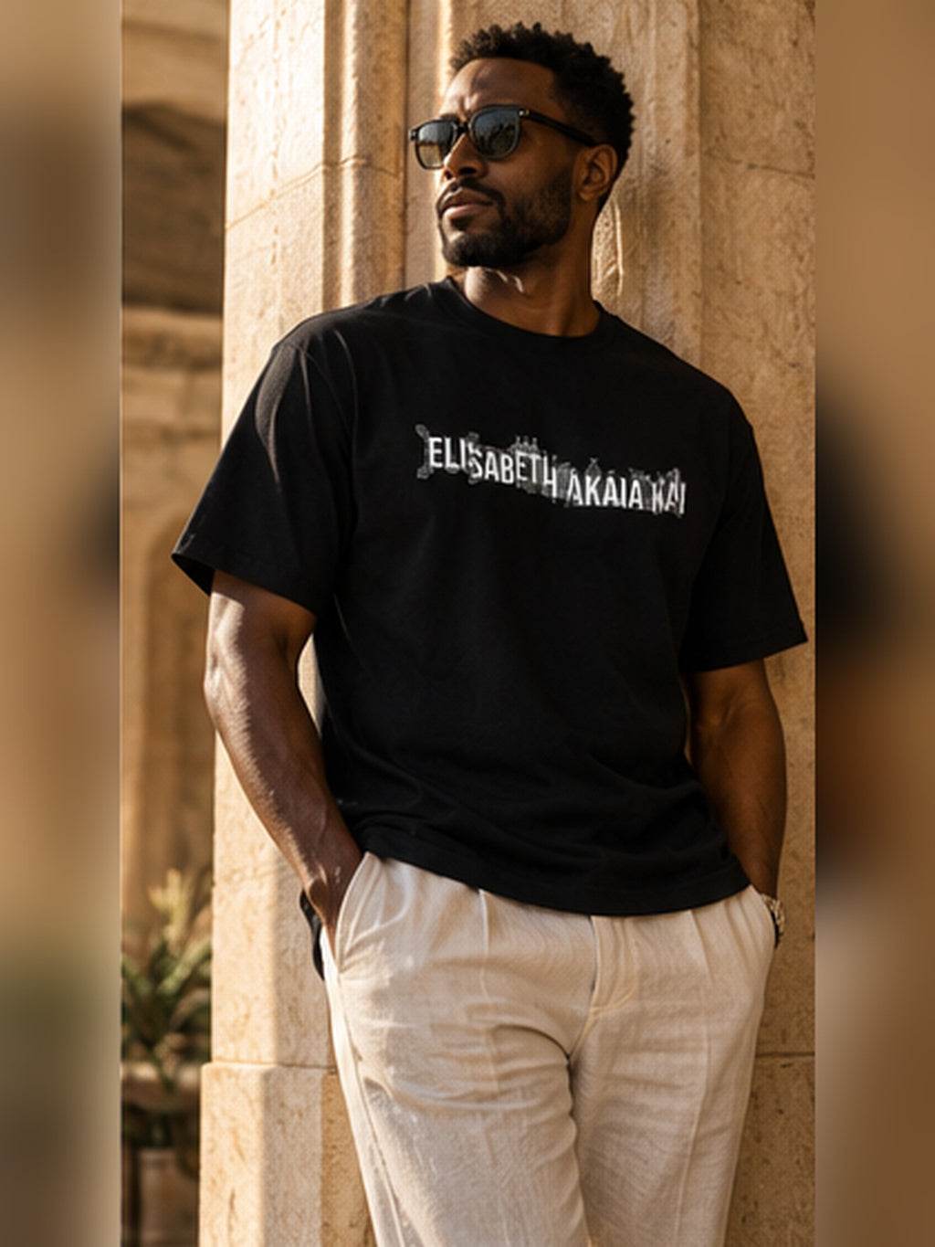 Homme portant le t-shirt KAÏ noir à signature blanche avec un pantalon clair, près d'une colonne en pierre dans un décor luxueux.