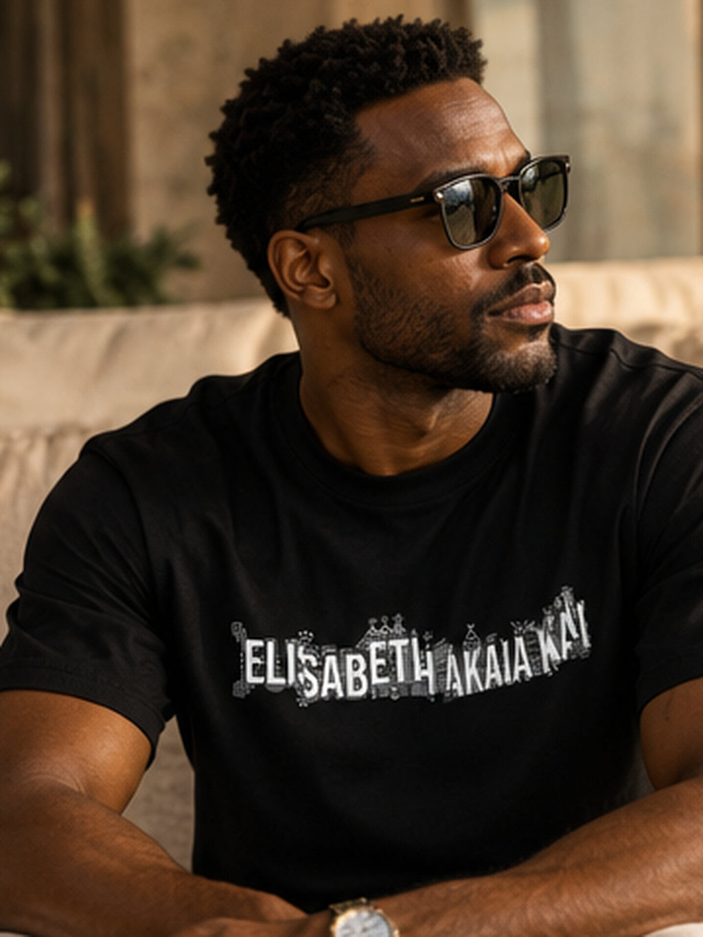 Portrait d'un homme portant le t-shirt de créateur KAÏ noir, assis dans un salon contemporain aux tons pierre et beige.