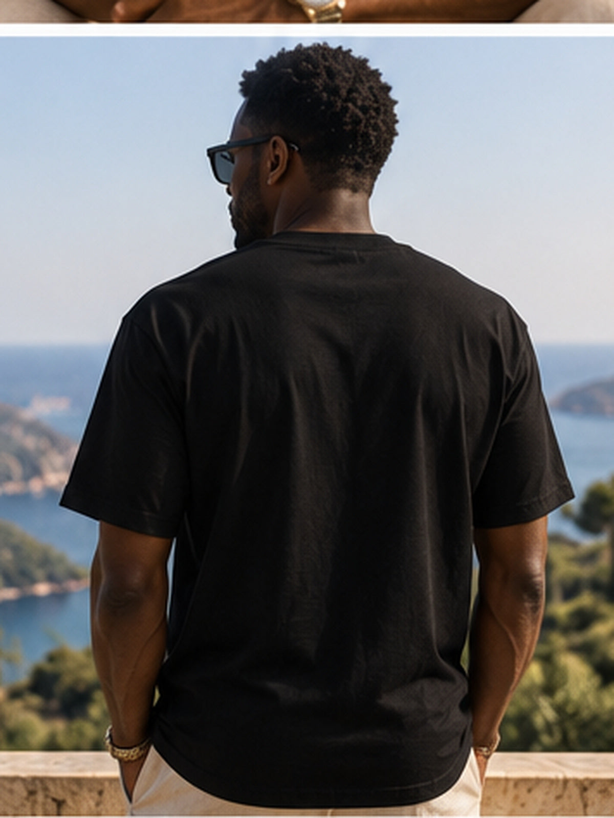 Vue de dos du t-shirt KAÏ noir à manches courtes porté par un homme sur une terrasse avec panorama côtier, dos uni sans imprimé.