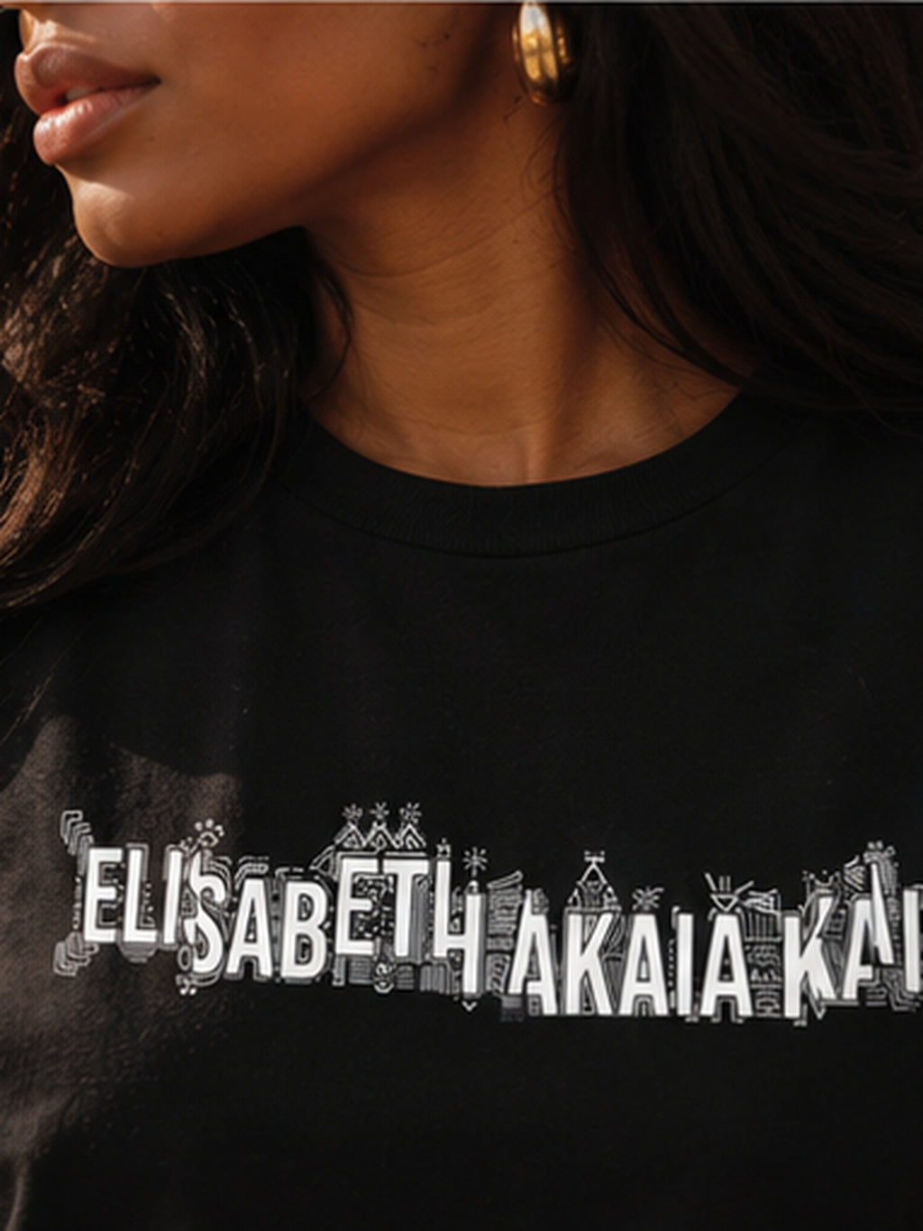 Gros plan sur l'imprimé graphique blanc du t-shirt KAÏ noir pour femme, signature de la Maison Élisabeth Akaïa Kaï.