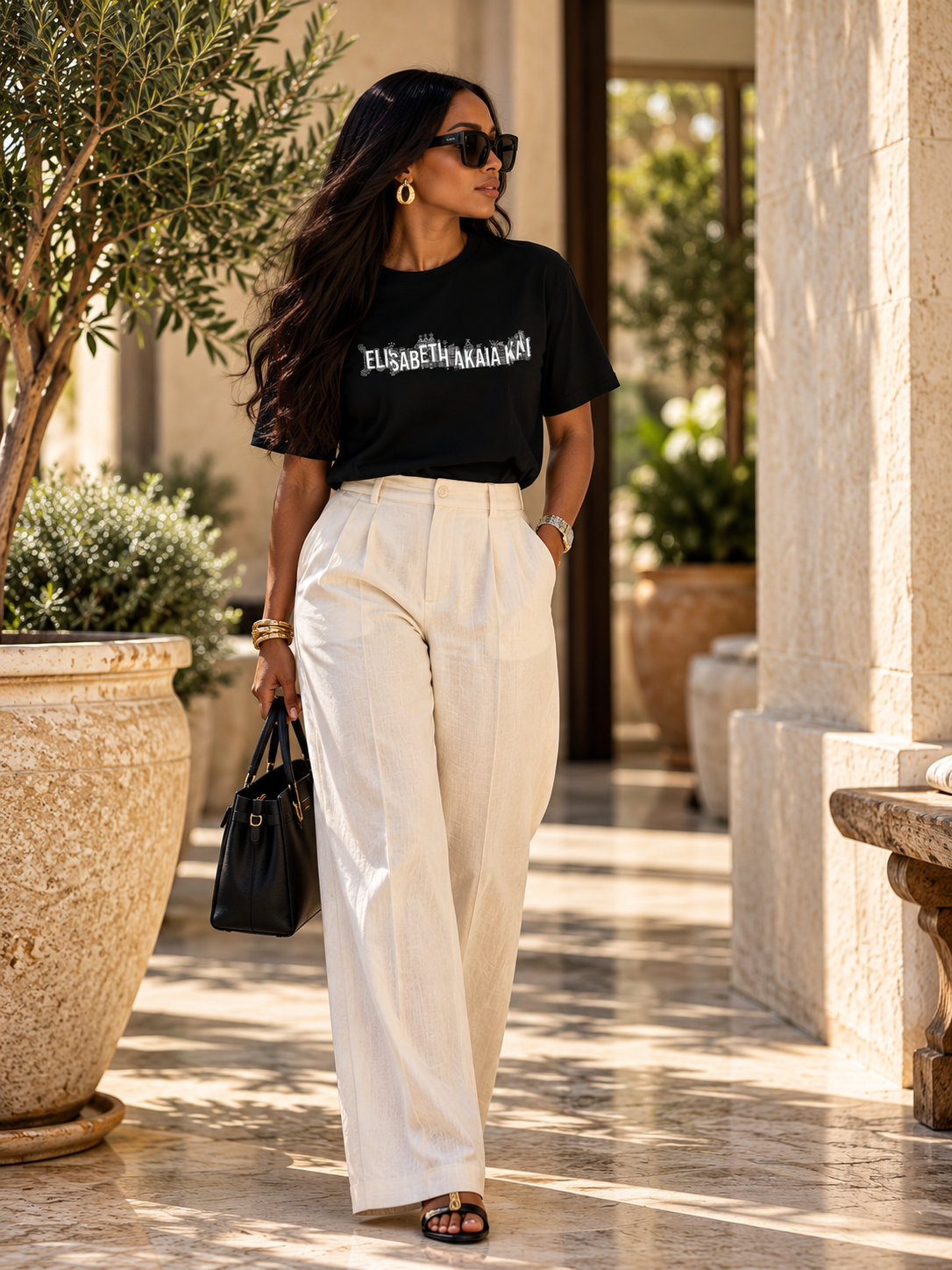 Mannequin femme portant le t-shirt KAÏ noir et un pantalon fluide ivoire dans un décor méditerranéen élégant, à la lumière naturelle.