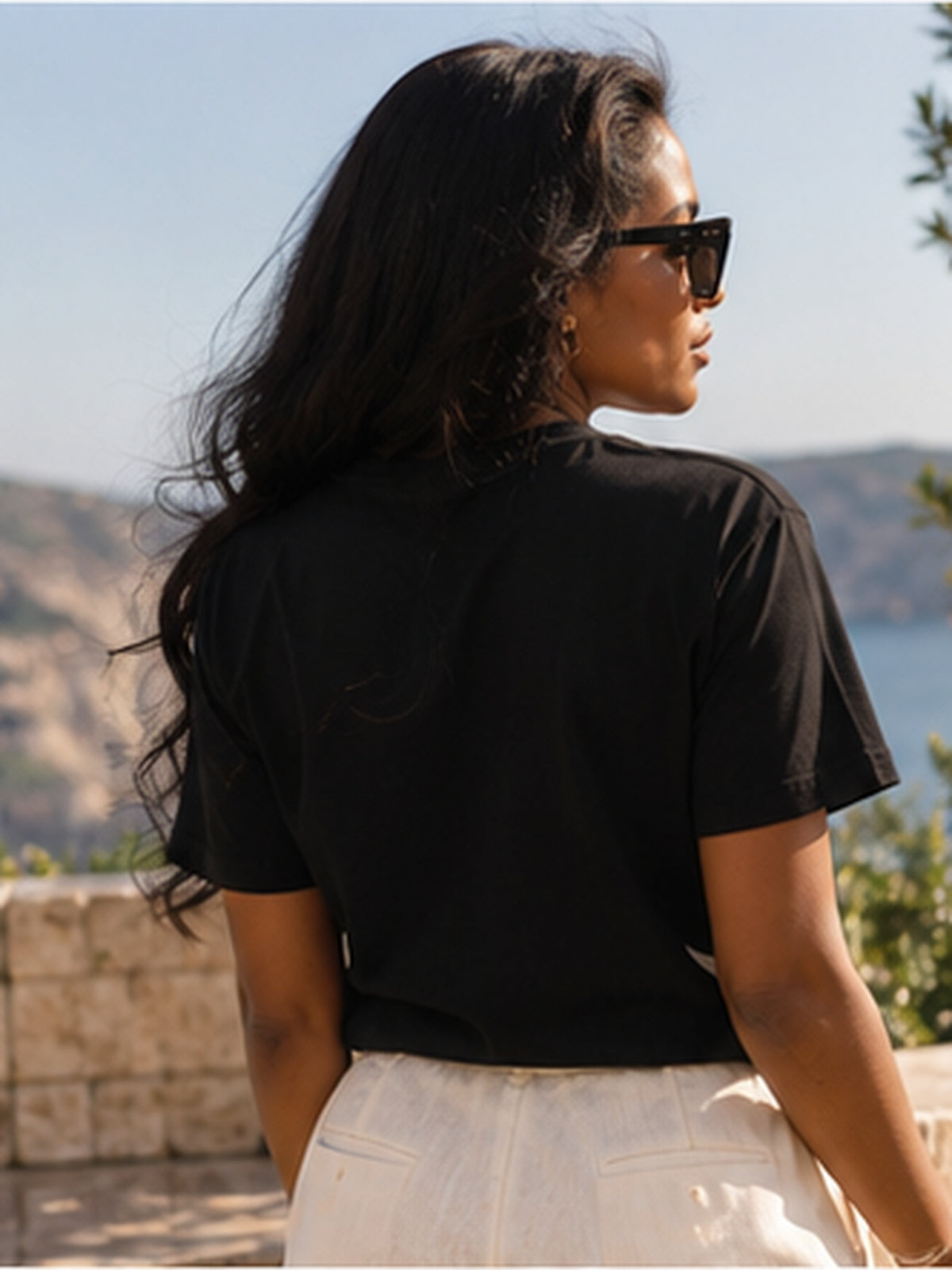 Vue de dos du t-shirt KAÏ noir porté par une femme sur une terrasse, montrant les manches courtes et le dos uni du vêtement.