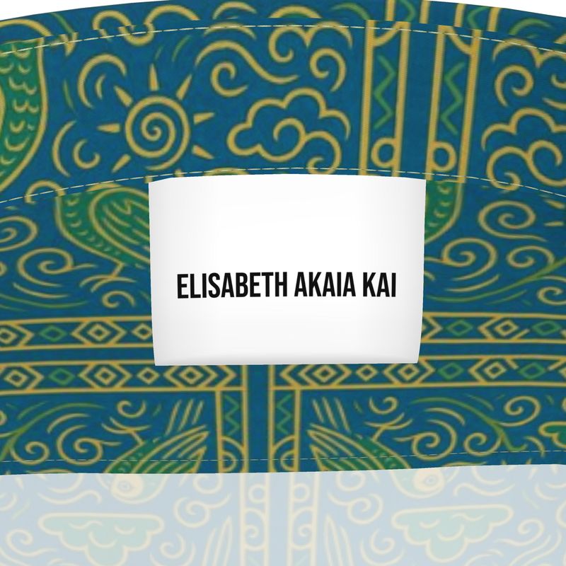 Vue rapprochée de l’étiquette blanche “Élisabeth Akaïa Kaï” sur fond d’imprimé vert émeraude et or, symboles solaires et motifs artistiques gabonais.